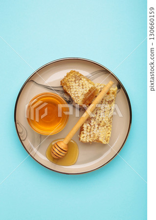 Bowl of sweet honey, dippers and combs on plate on blue background. Vertical photo 130660159