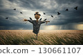 Scarecrow stands in wheat field with birds flying. 130661107