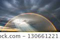 Rainbow arcs across stormy sky with sunlight breaking through. 130661221