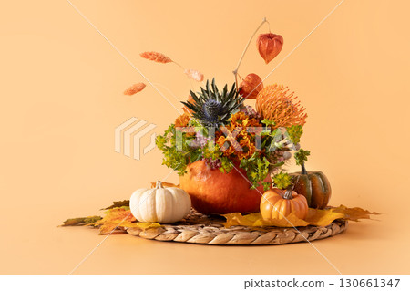 Autumn bouquet with orange and yellow flowers in pumpkin vase on orange background for Thanksgiving Day. Beautiful creative floral composition. Copy space. 130661347