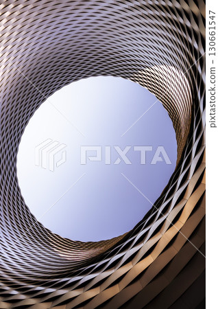 Geometric abstraction in the form of an ellipse made of different metal strips, around a circular air space. Vertical photo. 130661547