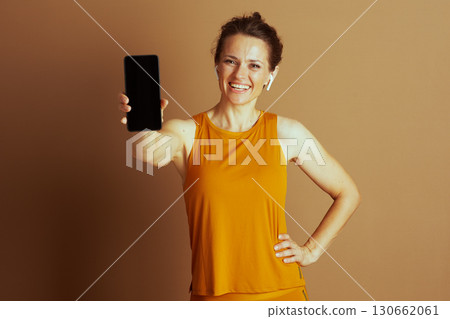 Cheerful Woman Presenting Phone in Athletic Wear Cheerful Woman Presenting Phone in Athletic Wear 130662061