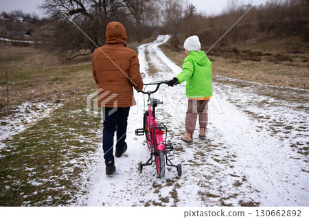 Walking together with a bright pink bicycle along a snowy path on a chilly winter day in a tranquil countryside setting 130662892