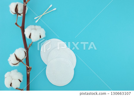 Cotton branch with fluffy flowers and cotton pads on left side of blue background, right side empty for copy space. Minimal, clean, natural composition 130663107