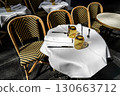 A set table of a street restaurant with a white tablecloth stands waiting for customers, surrounded by other empty tables and wicker chairs. Horizontal color photo 130663712