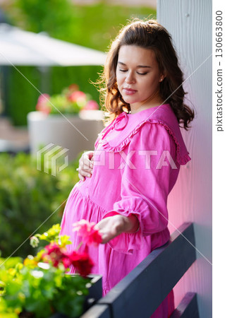 Beautiful young pregnant woman in pink dress on summer veranda.  130663800