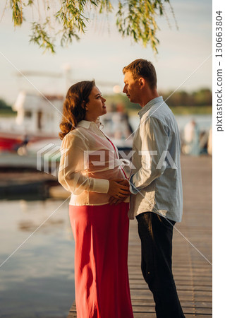 man and pregnant woman in red dress at sunset on the pier man and pregnant woman in red dress at sunset on the pier 130663804