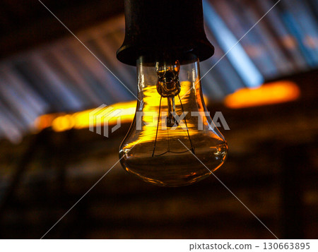 An incandescent lamp in the rays of the sun in a dark barn. An incandescent lamp in the rays of the sun in a dark barn. 130663895