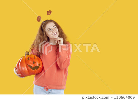 Happy woman with Halloween pumpkin looking away and thinking on yellow copy space background Happy woman with Halloween pumpkin looking away and thinking on yellow copy space background 130664009