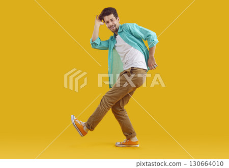 Full length portrait of dancing funky funny man in turquoise shirt on yellow background. Full length portrait of dancing funky funny man in turquoise shirt on yellow background. 130664010