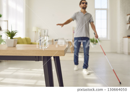 Blind man with stick is walking towards table with glass of water in living room Blind man with stick is walking towards table with glass of water in living room 130664050