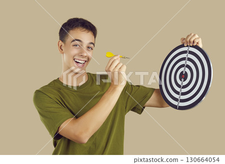Happy teenage boy focuses on achieving his goals and aims little arrow at target board 130664054