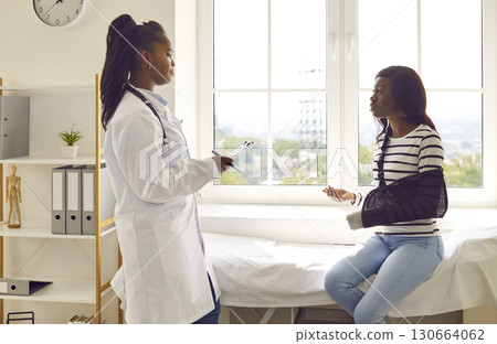 Doctor with clipboard and patient with sling on broken arm discussing treatment at clinic Doctor with clipboard and patient with sling on broken arm discussing treatment at clinic 130664062