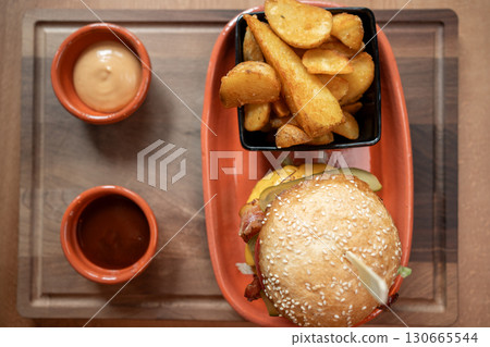 Delicious burger and crispy potato wedges served on a wooden platter Delicious burger and crispy potato wedges served on a wooden platter 130665544