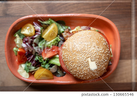 Delicious gourmet burger served with fresh garden salad on wooden table Delicious gourmet burger served with fresh garden salad on wooden table 130665546