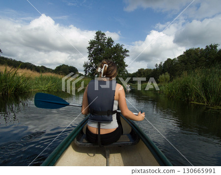 A young woman seen from behind canoeing in a river. Dark summer clouds in the background A young woman seen from behind canoeing in a river. Dark summer clouds in the background 130665991