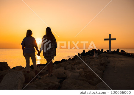Two women holding hands at sunrise near the large white cross monument on the pier in Varna, Bulgaria 130666000