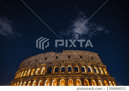 Colosseum illuminated at night with glowing arches under dark blue sky 130666031