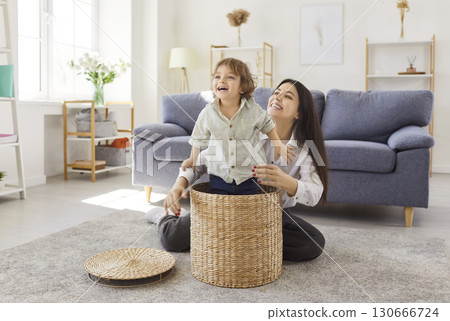 Mother having fun in the living room at home together with cute child boy playing with basket. Mother having fun in the living room at home together with cute child boy playing with basket. 130666724