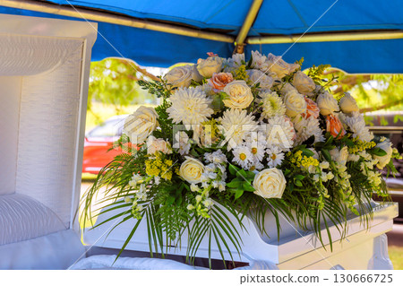 Assortment of flowers rests on casket during memorial service under serene canopy on sunny day. 130666725