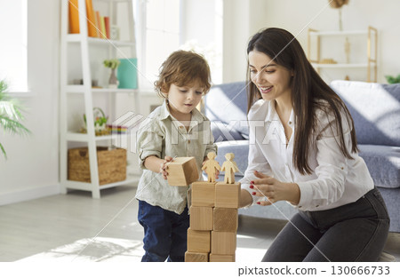 Mother and little son building tower of wooden blocks together, playing educational game at home. 130666733