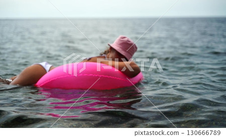 Lake Tubing Relaxation: Woman floats, enjoying summer lake relaxation on pink tube. 130666789