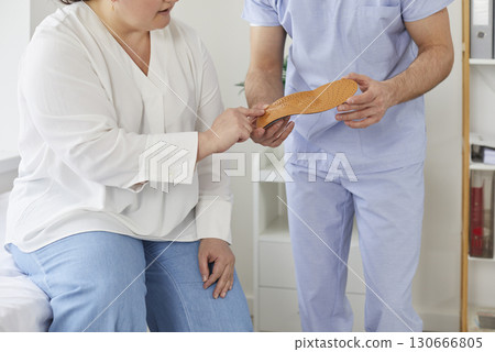 Chubby woman in clinic with help of doctor chooses new shoe insoles to improve her posture. 130666805