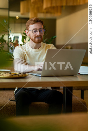 Ginger man professional using laptop at restaurant with pizza Ginger man professional using laptop at restaurant with pizza 130666926