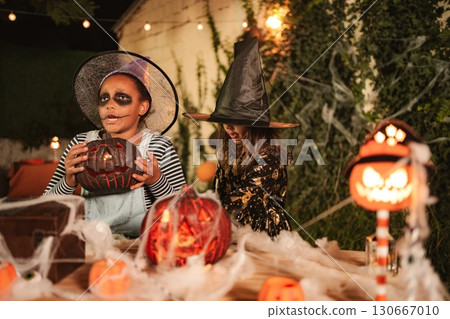 Two young girls wearing Halloween costumes playing with carved pumpkins and spiderwebs Two young girls wearing Halloween costumes playing with carved pumpkins and spiderwebs 130667010