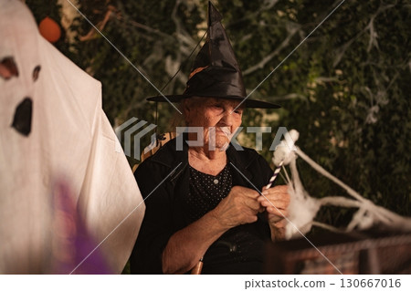 Senior woman making Halloween decorations wearing witch hat 130667016