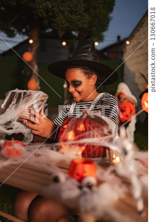 Young girl wearing witch costume opening gift at Halloween party 130667018