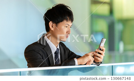 男商人一邊看著智慧型手機螢幕一邊思考 男商人一邊看著智慧型手機螢幕一邊思考 130667148