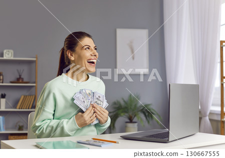 Happy woman with a wad of money sitting at home near a laptop Happy woman with a wad of money sitting at home near a laptop 130667555
