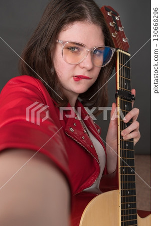 Female influencer guitarist biting her lip in playful expression takes selfie of herself with guitar in her hand, creating user-generated content Female influencer guitarist biting her lip in playful expression takes selfie of herself with guitar in her hand, creating user-generated content 130668296