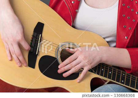 Cropped close-up view of guitar body and hands of female guitarist in relaxed position during break in performance 130668308