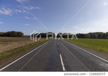 a highway with asphalt and white marking lines in autumn, a landscape with a highway and a forest on the horizon, blue sky in the autumn season 130668557