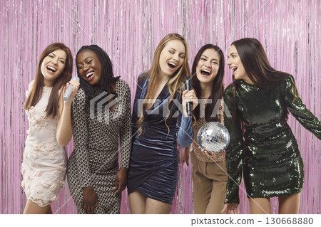 Female friends party together singing into microphones, women laughing, having fun, disco ball Female friends party together singing into microphones, women laughing, having fun, disco ball 130668880