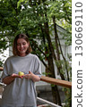 Smiling woman stands on a veranda in Peredelkino, looking down at a green apple gently held in her cupped hands 130669110