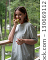 Smiling woman with short hair and silver earrings holding a green apple on a forest balcony, enjoying a moment of joy 130669112