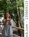 Woman gently presenting a green apple in her cupped hands, smiling with greenery in the background 130669115