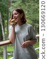 Smiling woman with short hair and silver earrings holding a green apple on a forest balcony, enjoying a moment of joy 130669120