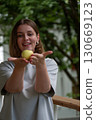 Woman gently presenting a green apple in her cupped hands, smiling with greenery in the background 130669123