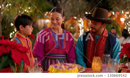 Family celebration with traditional attire and festive decorations during a joyful gathering at night. Mexican Posada celebration. Family celebration with traditional attire and festive decorations during a joyful gathering at night. Mexican Posada celebration. 130669542