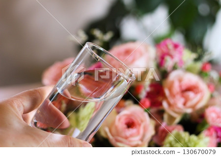 Hands holding a glass of water, a gorgeous bouquet of flowers, an image of water on flowers 130670079