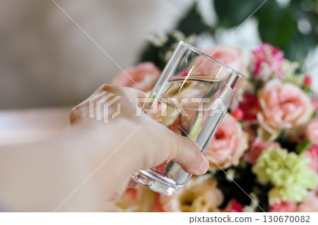 Hands holding a glass of water, a gorgeous bouquet of flowers, an image of water on flowers 130670082