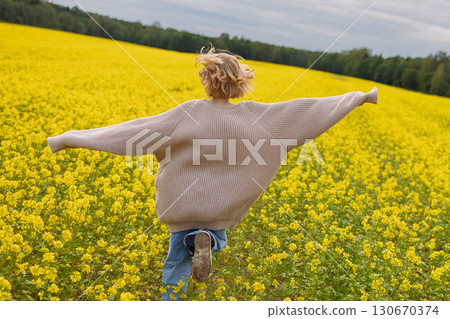Rear view of 10 year old girl in beige sweater running in yellow rapeseed field Rear view of 10 year old girl in beige sweater running in yellow rapeseed field 130670374