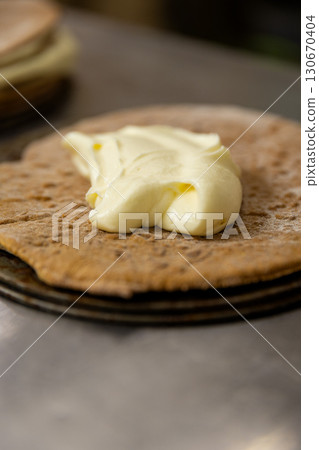 Spreading cream on cake layer, close-up view of dessert preparation in bakery kitchen Spreading cream on cake layer, close-up view of dessert preparation in bakery kitchen 130670404