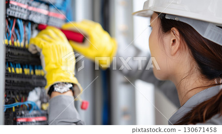 A female worker is maintaining a switchboard at a site 130671458