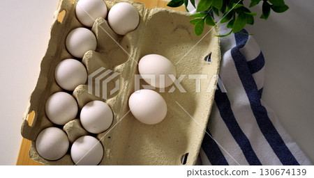 Closeup sequence of a hand taking fresh white eggs from a cardboard egg carton on wooden table with striped towel, top view cooking preparation scene. Closeup sequence of a hand taking fresh white eggs from a cardboard egg carton on wooden table with striped towel, top view cooking preparation scene. 130674139