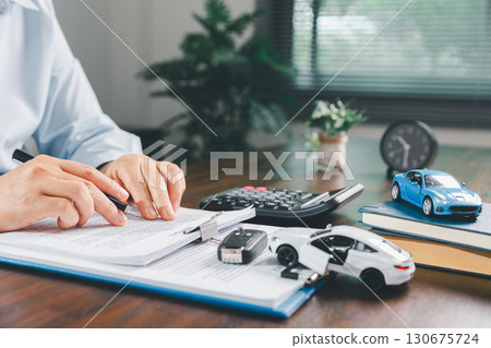 Businesswoman signing car insurance document or lease paper. Writing signature on contract or agreement. Buying or selling new or used vehicle. Car keys on table. Warranty or guarantee. 130675724